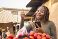 excited beautiful young african woman in a local african market using her smartphone giving thumbs up Royalty Free Stock Photo