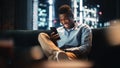 Excited Black African American Man Using Smartphone While Sitting on a Sofa in Living Room. Happy Royalty Free Stock Photo
