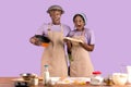 Excited black couple cooking together, holding homemade dough on violet studio background Royalty Free Stock Photo