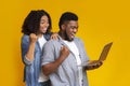 Excited black couple holding laptop, celebrating success with raised fists