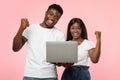 Excited black couple using laptop celebrating success shaking fists