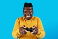 Excited black guy playing video games with joystick over blue background Royalty Free Stock Photo