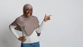 Excited black islamic woman pointing aside at copy space on light background