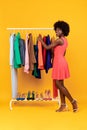 Black Lady Choosing Clothes Enjoying Shopping Over Yellow Background, Vertical