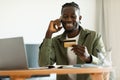 Excited black man holding credit card, having phone conversation with bank representative, sitting at home Royalty Free Stock Photo