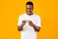 Excited Black Man Playing Games On Smartphone, Yellow Background