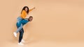 Excited black man piggybacking young wife, woman pointing finger at free copy space on peach studio background, panorama