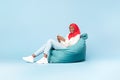 Excited black muslim woman in hijab using smartphone and smiling to camera, sitting in beanbag chair, blue background Royalty Free Stock Photo