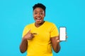 Excited Black Woman Pointing At Phone Screen Over Blue Background