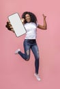 Excited black woman showing smarthone with blank white screen to camera, jumping with modern gadget, mockup