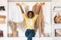 Excited Black Woman Sitting In Wardrobe Among New Clothes Indoor