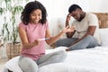 Excited black woman with pregnancy test next to frustrated man