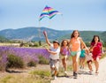 Excited boy flying rainbow kite with his friends Royalty Free Stock Photo