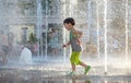 Excited boy having fun between water jets, in fountain. Summer i