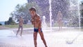 Excited boy of seven years having fun between water jets, in fountain, run around, sprinkle, have fun, have fun, on a