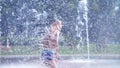 Excited boy of seven years having fun between water jets, in fountain, run around, sprinkle, have fun, have fun, on a