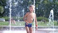 Excited boy of seven years having fun between water jets, in fountain, run around, sprinkle, have fun, have fun, on a