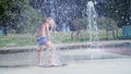 Excited boy of seven years having fun between water jets, in fountain, run around, sprinkle, have fun, have fun, on a