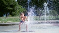 Excited boy of seven years having fun between water jets, in fountain, run around, sprinkle, have fun, have fun, on a