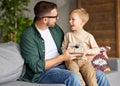 Excited boy son receiving gift box from young loving father on holiday while sitting together on sofa Royalty Free Stock Photo