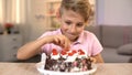 Excited boy taking cherry from top of delicious chocolate cake, birthday party