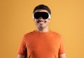 Excited brazilian man wearing vr vision pro glasses, using virtual reality for entertainment on orange studio background Royalty Free Stock Photo