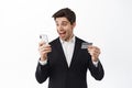 Excited businessman holding credit card, looking happy at smartphone screen, receive money transfer, standing over white