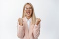 Excited businesswoman shouting and clenching fists, triumphing and celebrating success, standing in suit and glasses Royalty Free Stock Photo