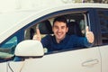 Excited casual guy sitting behind the steering wheel of the car showing thumbs up gesture as has passed the exam and obtain driver