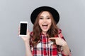 Excited casual woman pointing finger at blank screen mobile phone