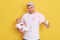 Excited Caucasian handsome young father feeding little newborn girl from bottle, man yelling happily, wearing white casual t shirt