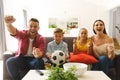 Excited caucasian parents on couch with daughter and son watching football match on tv and cheering