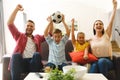 Excited caucasian parents on couch with daughter and son watching football match on tv and cheering