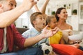 Excited caucasian parents on couch with daughter and son watching football match on tv and cheering