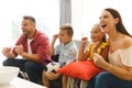 Excited caucasian parents on couch with daughter and son watching football match on tv and cheering