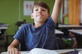 Excited caucasian schoolboy in classroom sitting at desk and raising hand Royalty Free Stock Photo