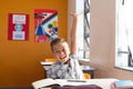 Excited caucasian schoolboy sitting at desk in classroom raising hand during lesson Royalty Free Stock Photo