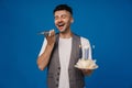 Excited man holding birthday cake and talking on mobile phone isolated over blue wall Royalty Free Stock Photo