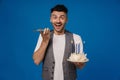 Excited man holding birthday cake and talking on mobile phone isolated over blue wall Royalty Free Stock Photo