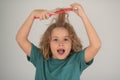 Excited child with curly blonde hair holding comb hairbrush for combing. Child with tangled blonde long hair tries to