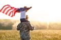 Excited child sitting with american flag on shoulders of father reunited with family