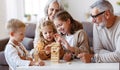 Excited children playing game Jenga at home with positive senior grandparents while sitting on sofa Royalty Free Stock Photo