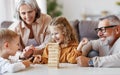 Excited children playing game Jenga at home with positive senior grandparents while sitting on sofa Royalty Free Stock Photo