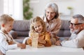 Excited children playing game Jenga at home with positive senior grandparents while sitting on sofa Royalty Free Stock Photo