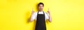 Excited coffee shop owner in black apron pointing fingers up, showing special offers, standing over yellow background