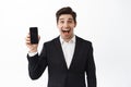 Excited corporate man introduce application, showing empty phone screen and scream from excitement and joy, standing in Royalty Free Stock Photo