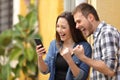 Excited couple finding online offers on phone in the street Royalty Free Stock Photo