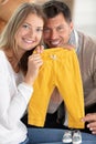 excited couple on sofa holding baby clothes Royalty Free Stock Photo