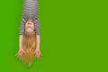 Excited crazy little blonde girl hanging happy upside down hands up over isolated green studio background. Emotion Royalty Free Stock Photo