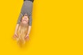 Excited crazy little blonde girl hanging happy upside down hands up over isolated yellow studio background. Emotion Royalty Free Stock Photo